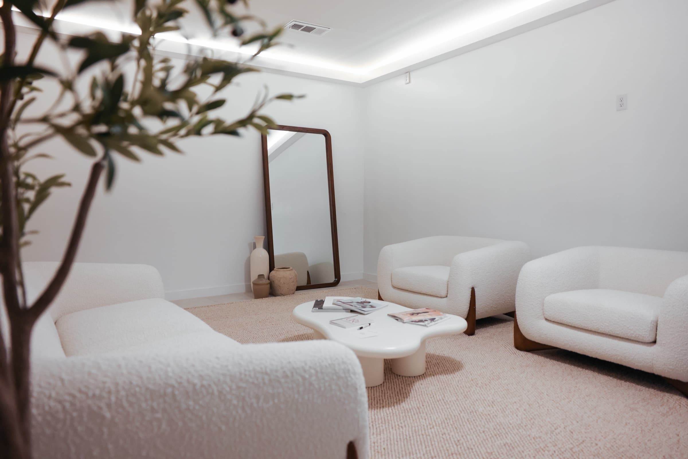 The lounge at Ora Medical Spa — boucle chairs around a low table beneath an olive tree